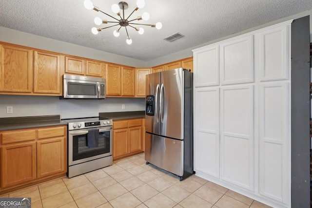 194 Retreat Pl, Woodbine, GA 31569 - kitchen featuring appliances with stainless steel finishes, dark countertops, light tile patterned floors, a textured ceiling, and a chandelier