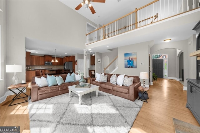 7049 Bennington Ln, Cumming, GA 30041 - living area featuring arched walkways, light wood finished floors, ceiling fan, a towering ceiling, and stairway