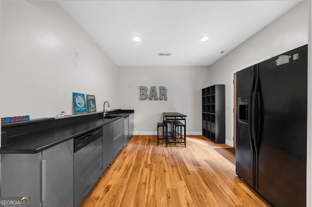 7049 Bennington Ln, Cumming, GA 30041 - kitchen with black fridge with ice dispenser, dishwasher, light wood-style flooring, dark countertops, and recessed lighting