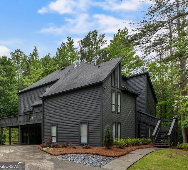 view of side of property featuring stairs, roof with shingles, a deck, asphalt driveway, and an attached garage