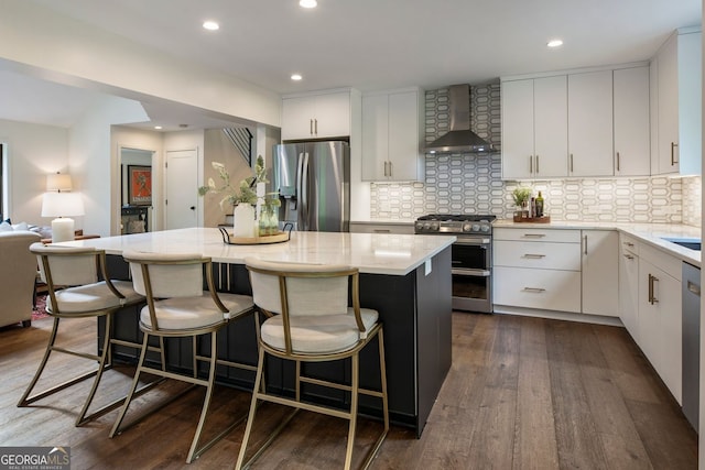 kitchen with appliances with stainless steel finishes, wall chimney range hood, a center island, tasteful backsplash, and white cabinetry