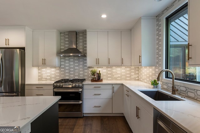 kitchen featuring appliances with stainless steel finishes, wall chimney range hood, a sink, dark wood-style floors, and light stone countertops