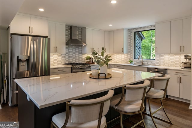 kitchen featuring wall chimney exhaust hood, appliances with stainless steel finishes, a sink, dark wood-type flooring, and a kitchen island