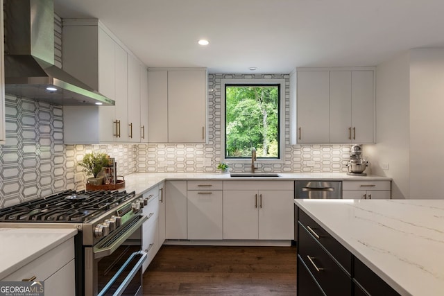 kitchen featuring stainless steel appliances, wall chimney exhaust hood, a sink, dark wood-style flooring, and decorative backsplash