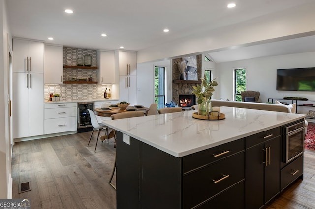 kitchen with beverage cooler, open shelves, open floor plan, a fireplace, and white cabinetry