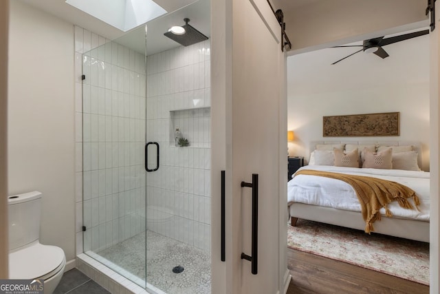 ensuite bathroom with a skylight, toilet, a shower stall, and a ceiling fan