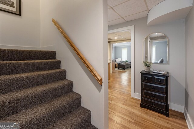 staircase with wood finished floors, arched walkways, a drop ceiling, and baseboards