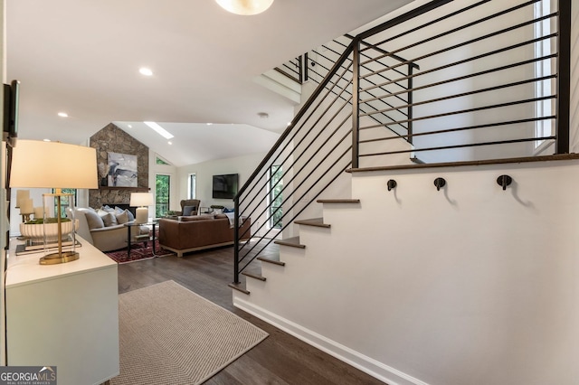 staircase featuring wood finished floors, baseboards, vaulted ceiling, a stone fireplace, and recessed lighting
