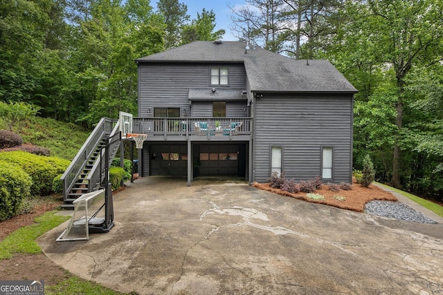 rear view of property with roof with shingles, stairway, driveway, an attached garage, and a deck