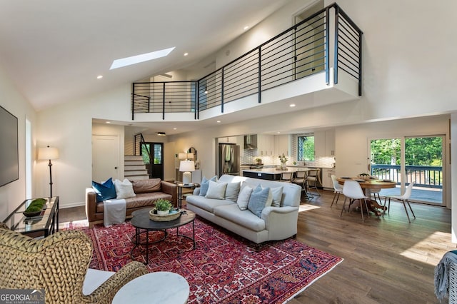 living room featuring stairway, high vaulted ceiling, dark wood-style flooring, a skylight, and recessed lighting