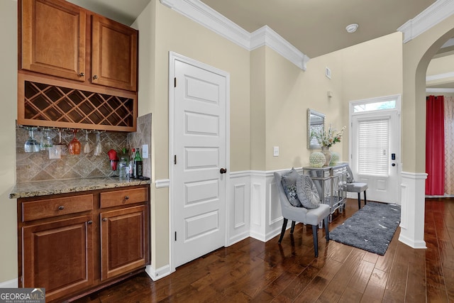4581 Sagebrush Ct, Snellville, GA 30039 - indoor dry bar featuring arched walkways, dark wood-type flooring, crown molding, decorative backsplash, and a wainscoted wall