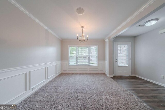 unfurnished dining area with a chandelier, crown molding, wainscoting, wood finished floors, and a decorative wall
