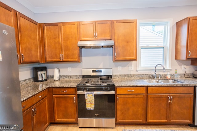 kitchen featuring stainless steel appliances, under cabinet range hood, a sink, light stone countertops, and brown cabinetry