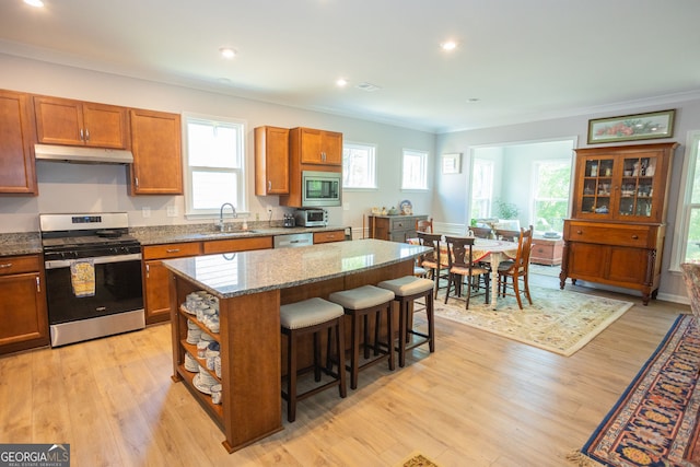 kitchen with stainless steel appliances, under cabinet range hood, a sink, brown cabinetry, and crown molding