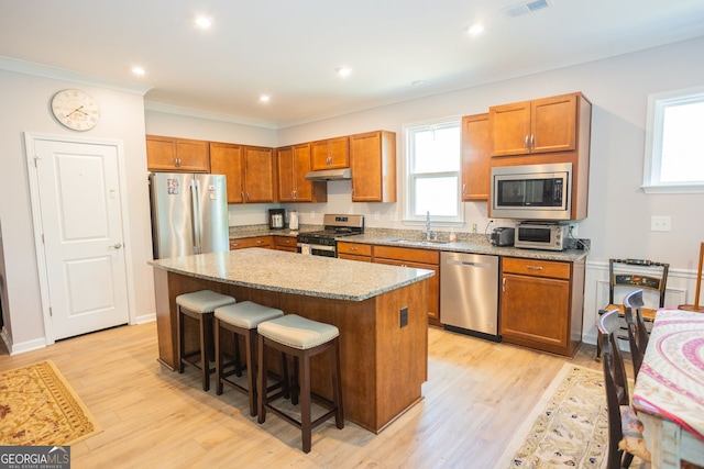 kitchen with stainless steel appliances, a sink, a kitchen island, a breakfast bar, and light wood finished floors