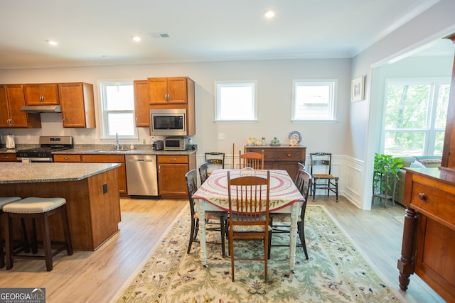 kitchen with stainless steel appliances, a sink, under cabinet range hood, brown cabinetry, and recessed lighting