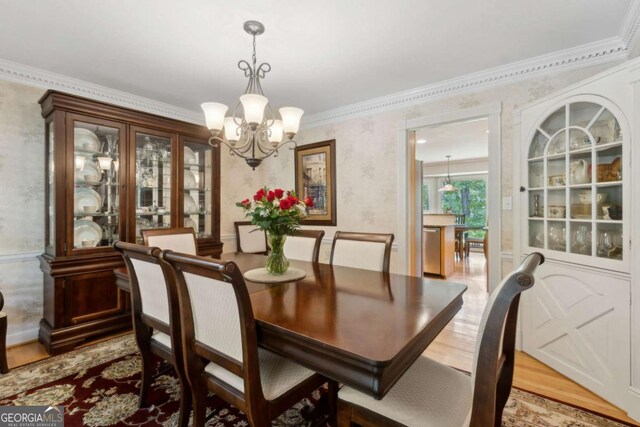 dining room featuring a chandelier, light wood finished floors, ornamental molding, and wallpapered walls
