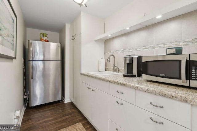 kitchen with stainless steel appliances, a sink, decorative backsplash, dark wood finished floors, and white cabinets