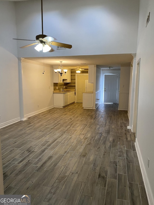 unfurnished living room featuring dark wood-style flooring, a ceiling fan, baseboards, a towering ceiling, and a chandelier