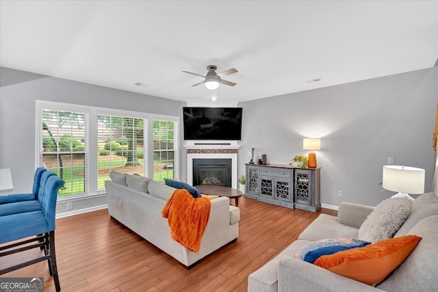 living room with baseboards, ceiling fan, wood finished floors, and a glass covered fireplace