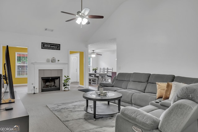 carpeted living area with a ceiling fan, high vaulted ceiling, a tiled fireplace, and baseboards