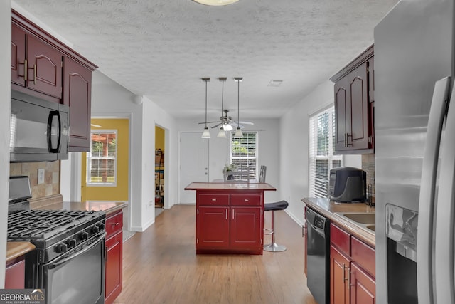 kitchen featuring black appliances, light wood-style flooring, baseboards, and a center island