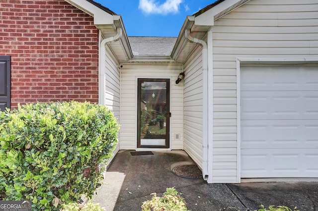 entrance to property featuring a garage, brick siding, and a shingled roof