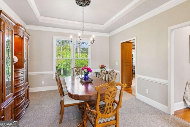 carpeted dining room with a chandelier, a raised ceiling, crown molding, and baseboards