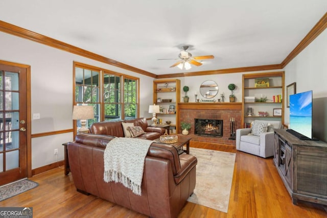 living area with ceiling fan, crown molding, wood finished floors, a brick fireplace, and baseboards