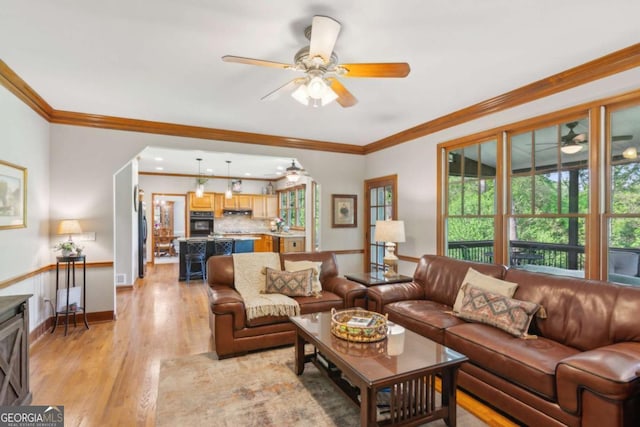 living room featuring a ceiling fan, light wood finished floors, crown molding, and baseboards
