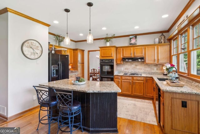 kitchen with black appliances, under cabinet range hood, a sink, light stone countertops, and ornamental molding