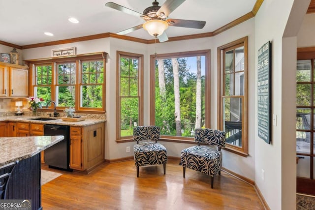 kitchen featuring black dishwasher, light wood-style flooring, a sink, ornamental molding, and light stone countertops