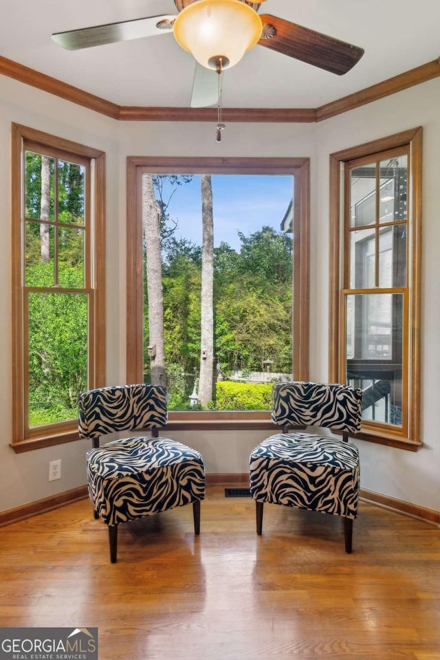 living area featuring plenty of natural light, wood finished floors, baseboards, and crown molding