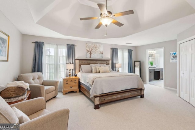 bedroom featuring light colored carpet, multiple windows, a raised ceiling, and ensuite bathroom