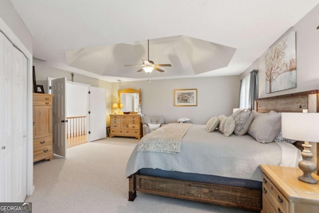 bedroom with light colored carpet, a raised ceiling, and a ceiling fan