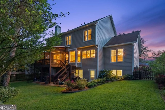 back of house at dusk featuring stairs, a chimney, and a wooden deck