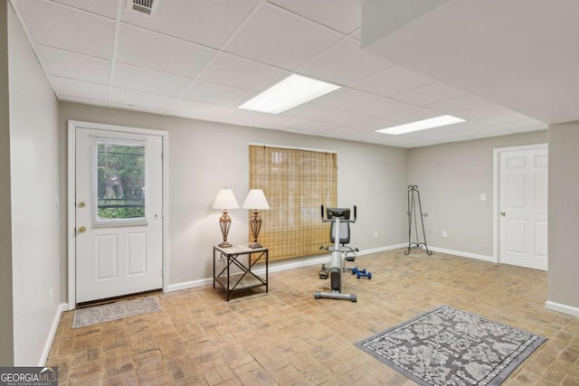 exercise room featuring baseboards, a drop ceiling, and brick patterned floors