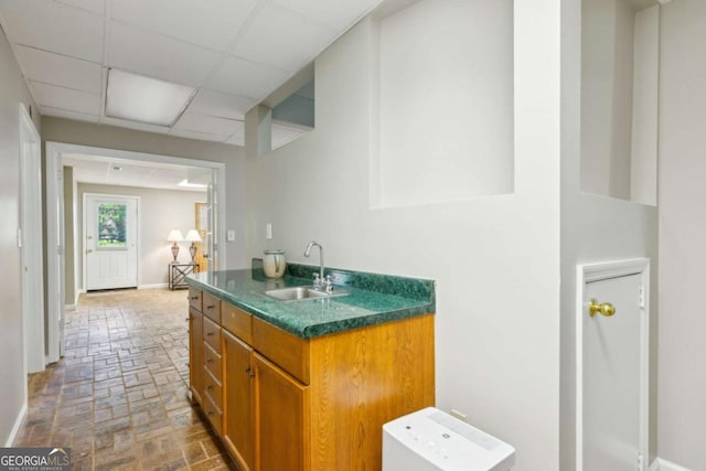 bathroom featuring a sink, brick patterned floors, a paneled ceiling, and baseboards