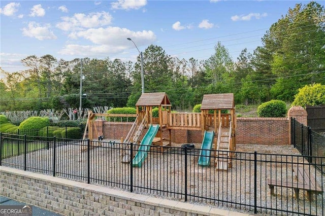 community jungle gym with fence and view of wooded area