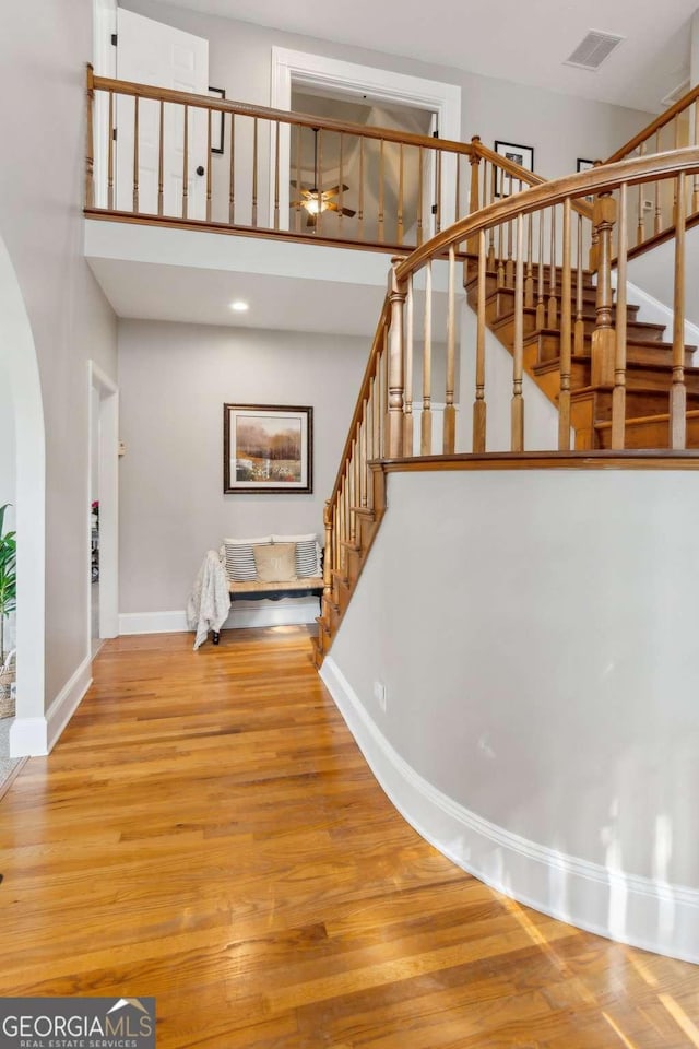 stairs with a towering ceiling, baseboards, wood finished floors, and arched walkways