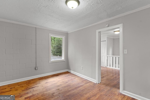 unfurnished room featuring a textured ceiling, hardwood / wood-style floors, crown molding, baseboards, and a smoke detector