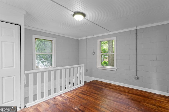 spare room featuring concrete block wall, wood finished floors, and ornamental molding