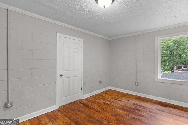 unfurnished room with hardwood / wood-style flooring, a textured ceiling, ornamental molding, baseboards, and concrete block wall