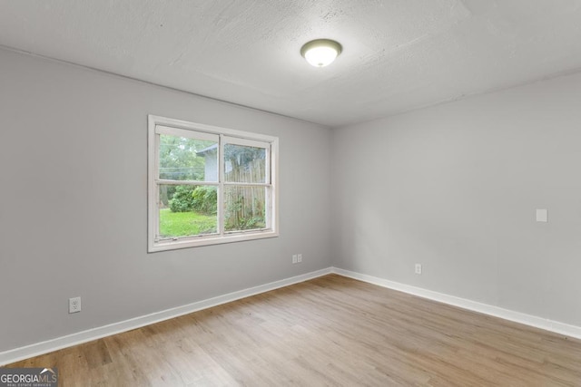 spare room featuring light wood-type flooring, baseboards, and a textured ceiling