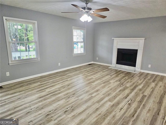 3045 Revere Cir, Snellville, GA 30039 - unfurnished living room featuring wood finished floors, healthy amount of natural light, a ceiling fan, a textured ceiling, and a fireplace with flush hearth