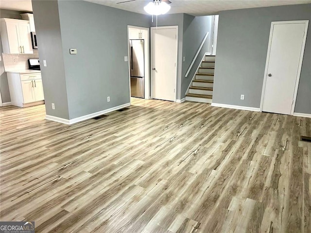 3045 Revere Cir, Snellville, GA 30039 - unfurnished living room featuring a ceiling fan, stairway, light wood-type flooring, and baseboards