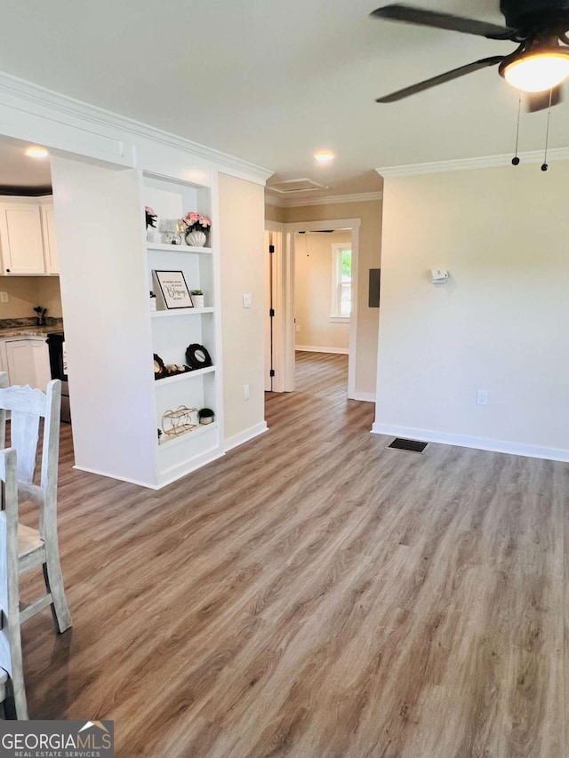 unfurnished living room featuring ornamental molding, ceiling fan, light wood-type flooring, built in shelves, and baseboards