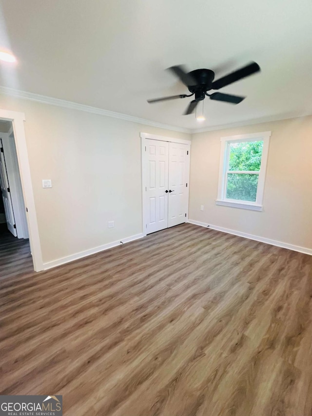 unfurnished bedroom with ornamental molding, wood finished floors, baseboards, a closet, and a ceiling fan