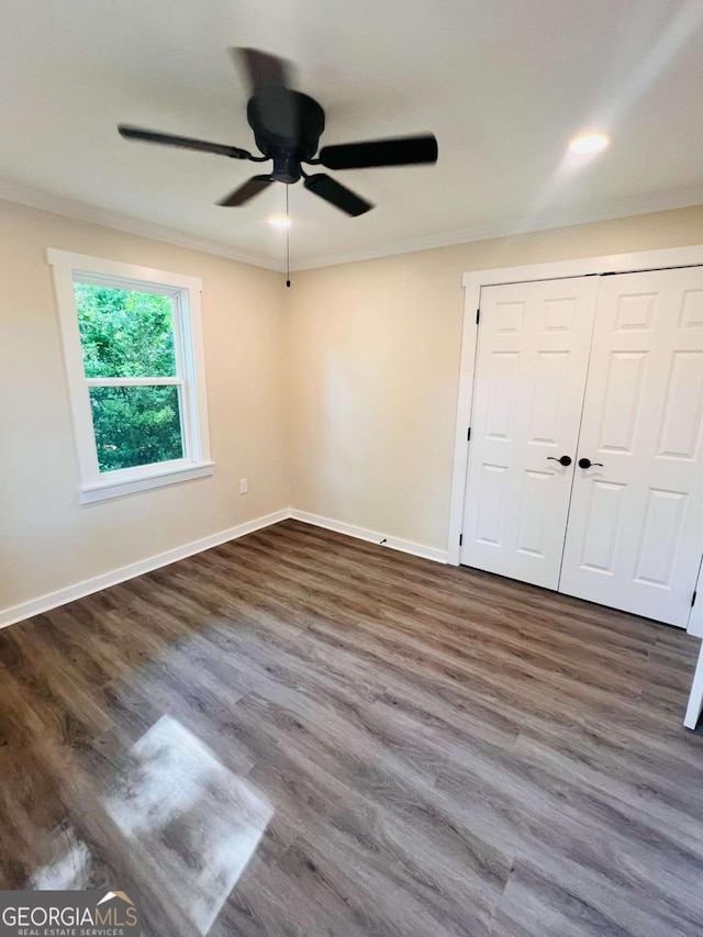 empty room with ceiling fan, dark wood finished floors, baseboards, and crown molding