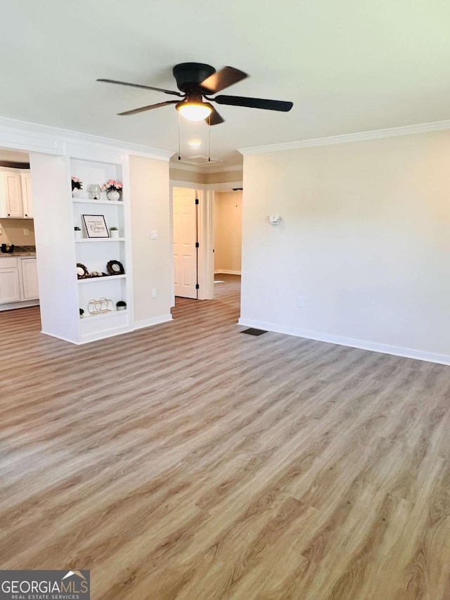 unfurnished living room with ornamental molding, a ceiling fan, light wood-type flooring, baseboards, and built in shelves